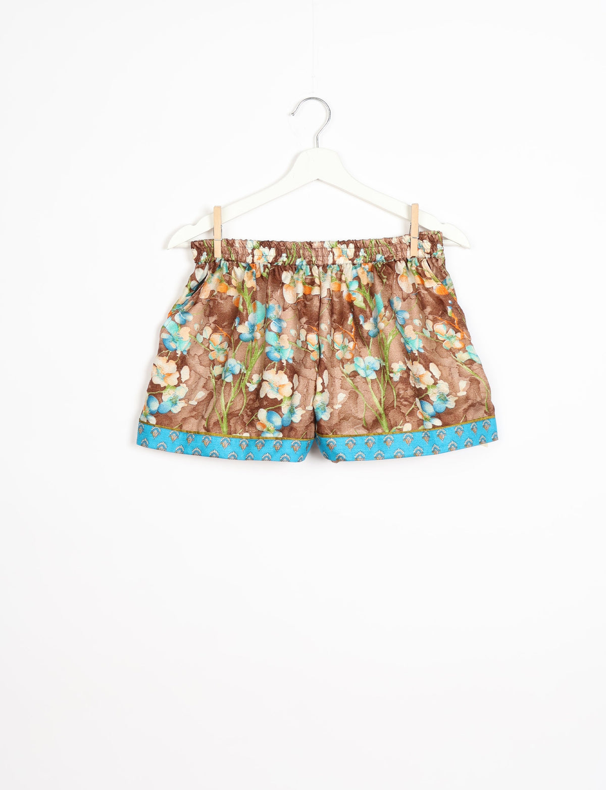 Brown floral print shorts with elastic waistband and blue patterned hem, hanging on white hanger against white background