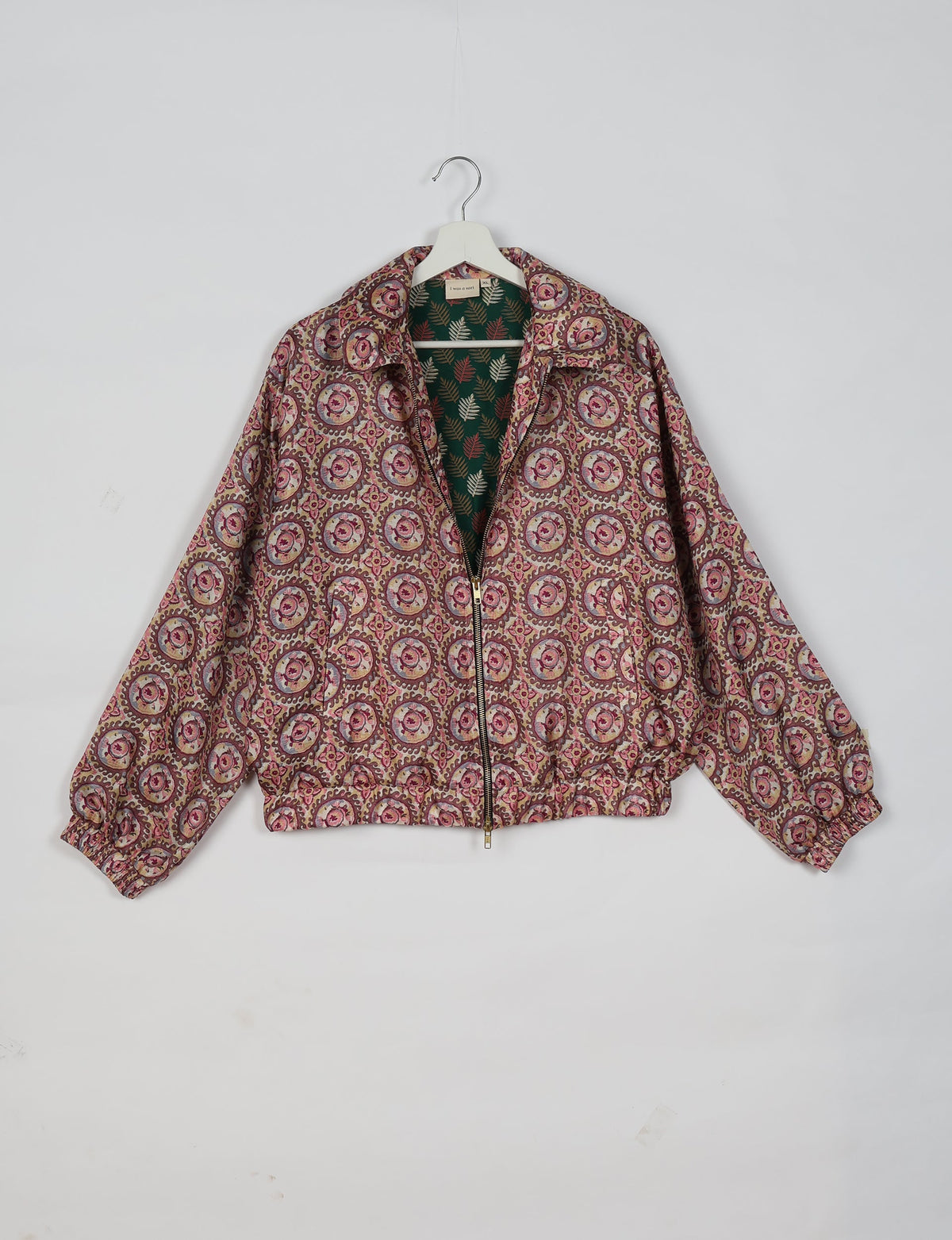 Bomber jacket in brown with circular floral pattern, zip front, elastic cuffs, and tropical leaf print lining, hanging on white hanger