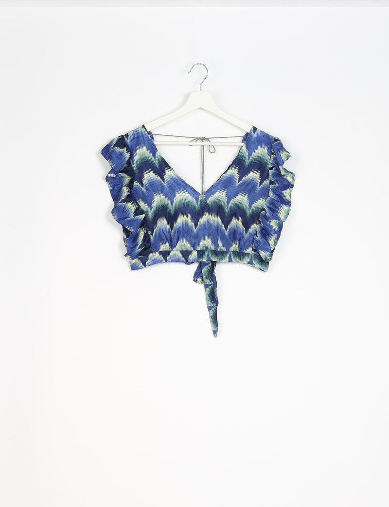 Blue ikat patterned cropped top with ruffled sleeves, V-neckline, back tie, and front tie detail hanging on white hanger
