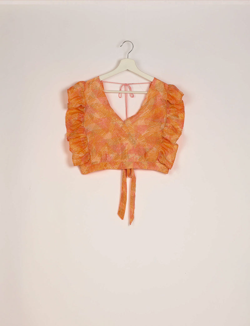 Orange abstract print cropped top with frill sleeves, V-neck, back tie closure, and front wrap detail hanging on white hanger