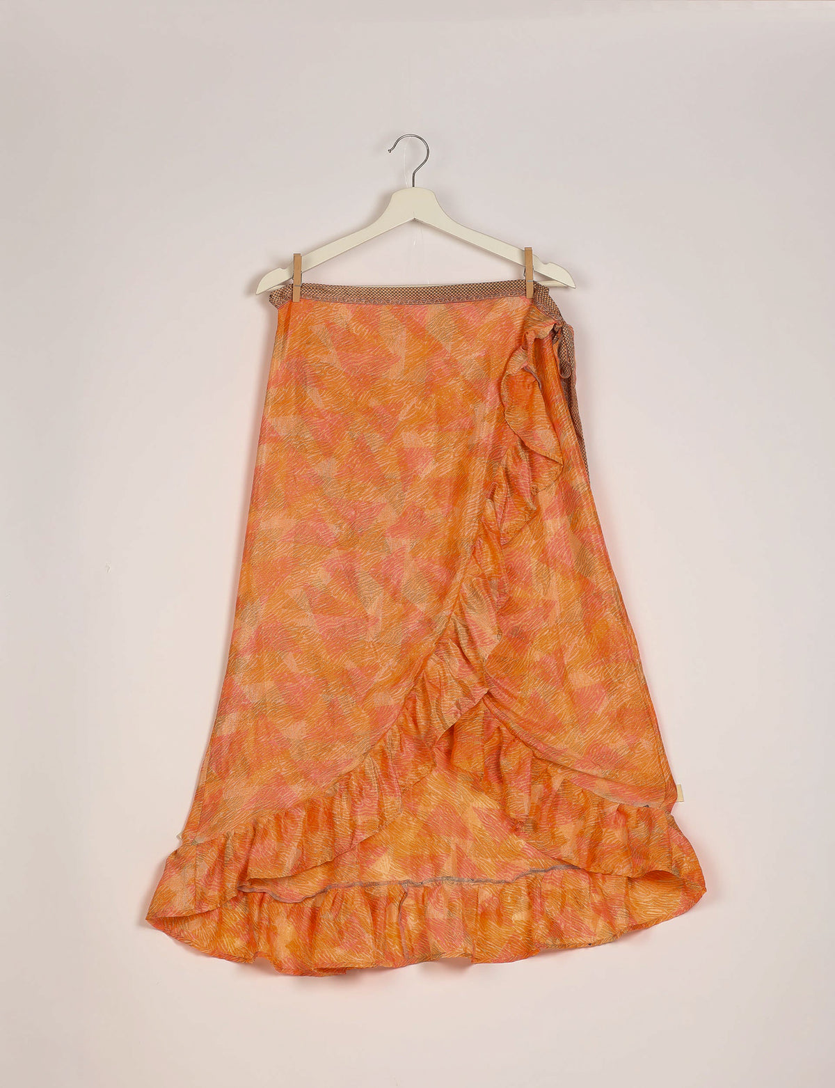 Orange abstract patterned skirt with ruffle trim hanging on white hanger against plain background