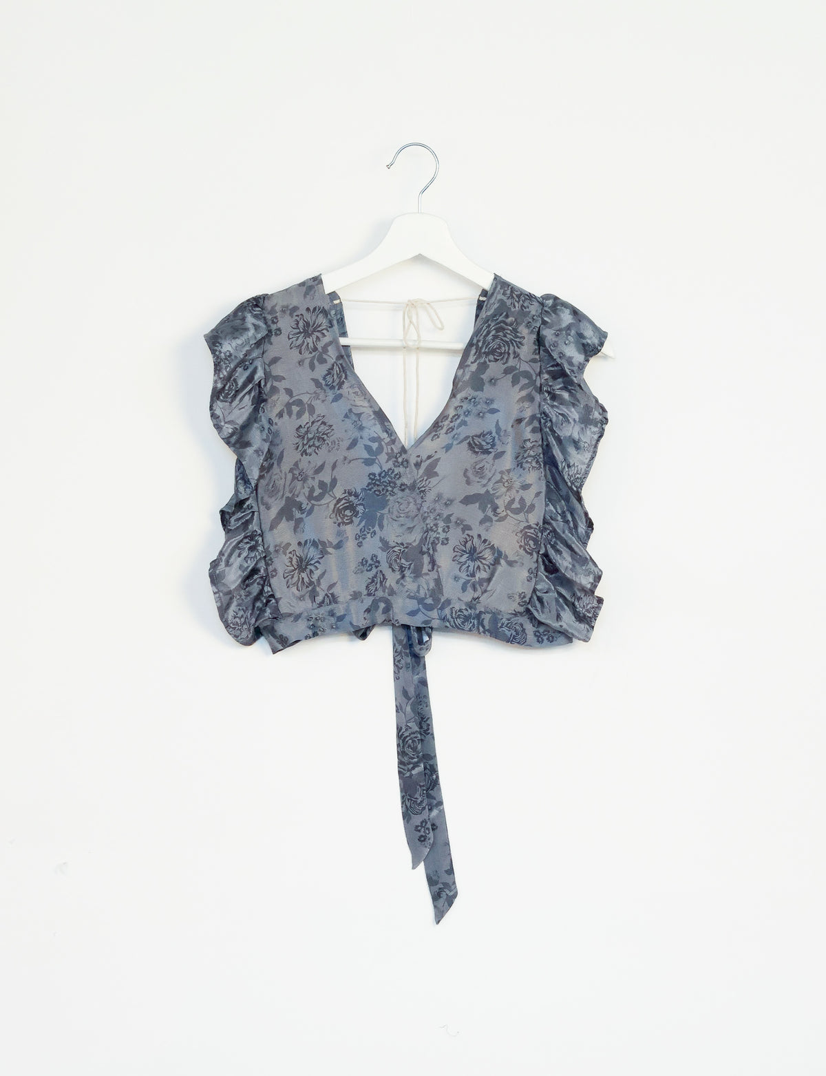 Grey tropical floral print frill sleeve crop top with V-neck and tie detail hanging on white hanger against white background