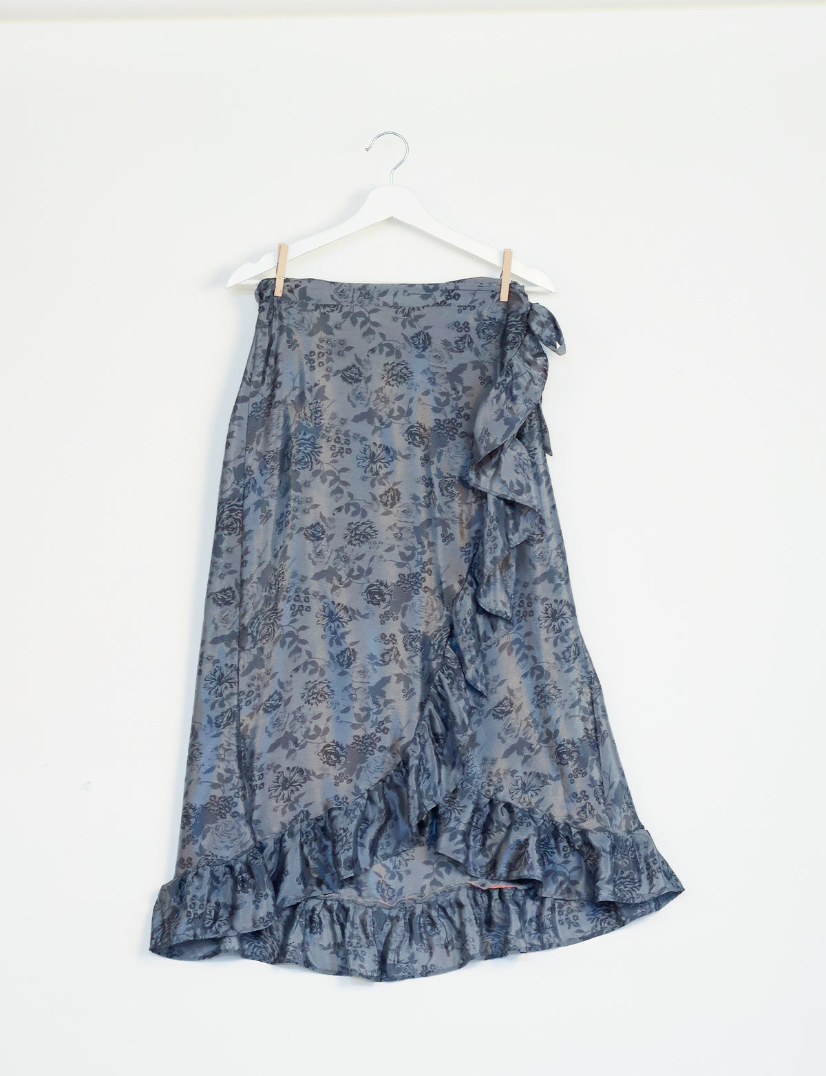 Grey tropical floral print skirt with ruffle trim and side tie, hanging on white hanger against white background