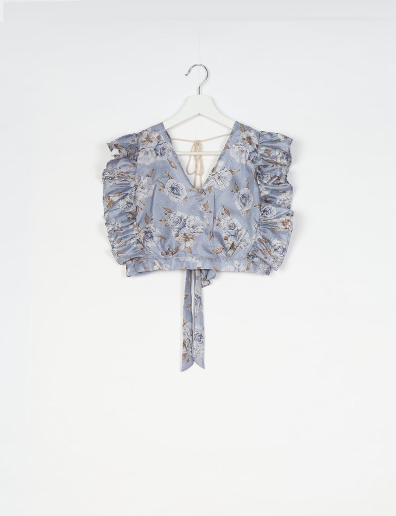 Grey floral crop top with frill sleeves, V-neck, and tie-back detail hanging on white hanger against white background