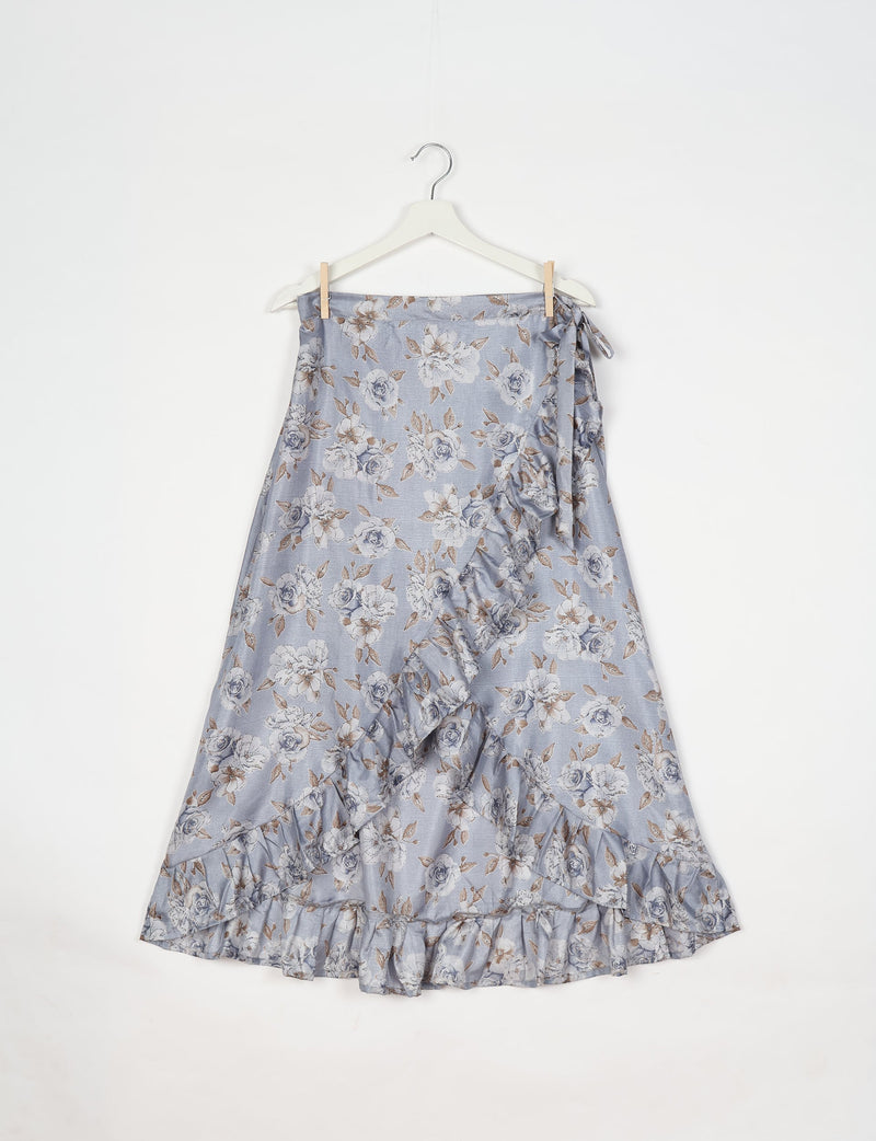 Grey floral wrap skirt with ruffle trim and side tie, hanging on white hanger against white background