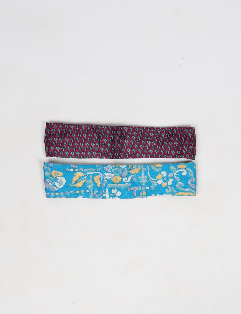 Set of two elastic headbands, one burgundy with small teal pattern, one blue with multicolor floral design, flat lay