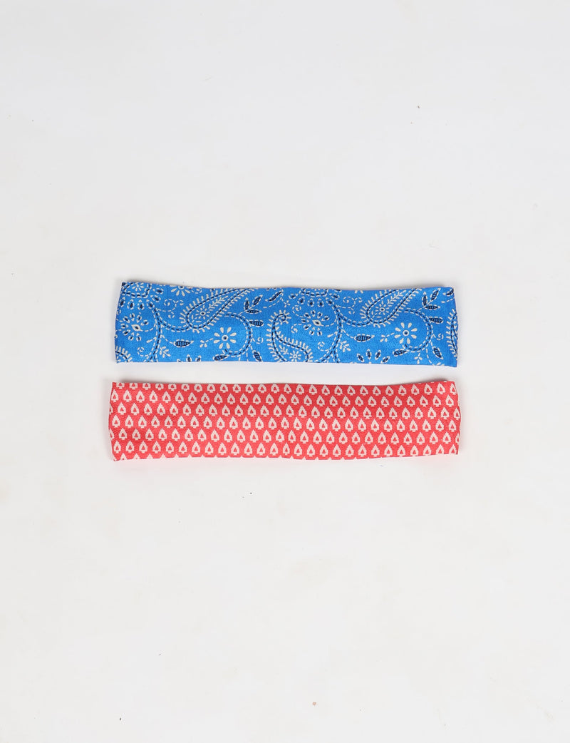 Set of two elastic headbands, one blue with white paisley pattern, one red with white teardrop pattern, flat lay view