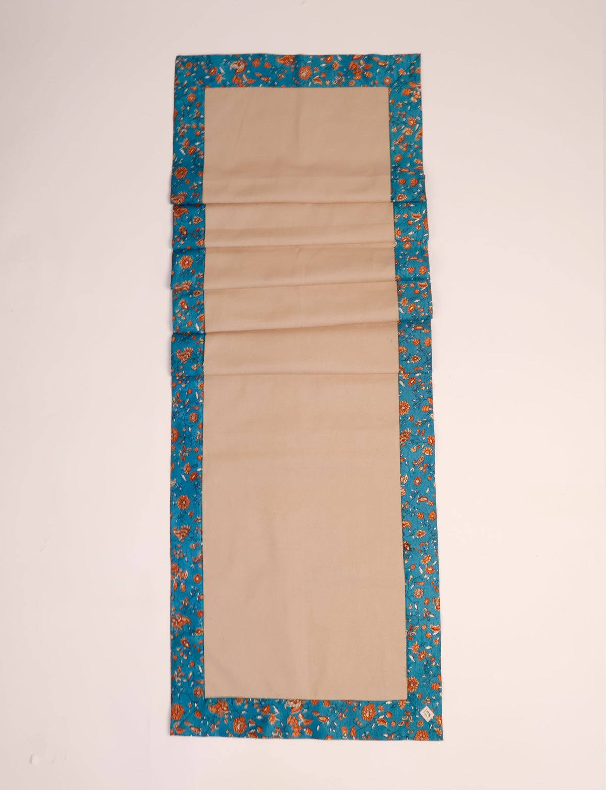 Beige table runner with blue tropical floral border, flat laid on a light background, small label on corner visible