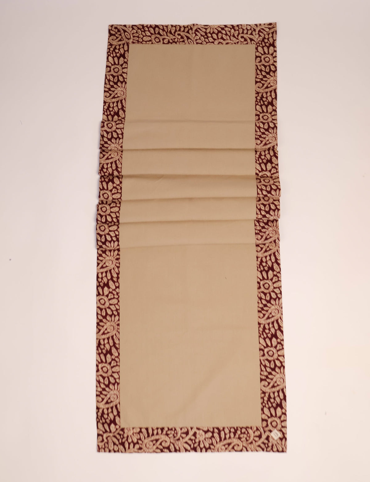 Beige table runner with dark red tropical floral patterned border, shown flat on a white surface