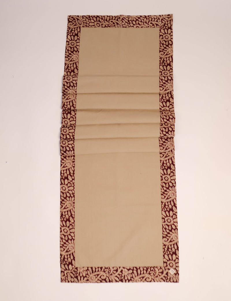 Beige table runner with dark red tropical floral patterned border, shown flat on a white surface