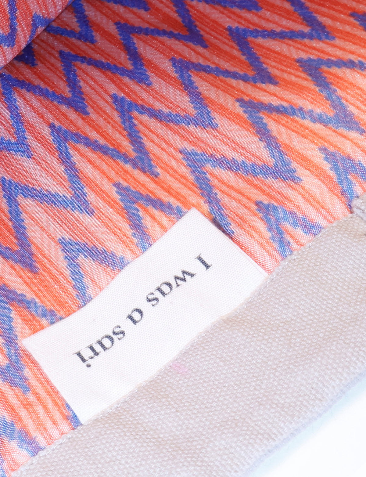 Orange fabric with blue zigzag geometric pattern and a white label partially visible on beige textured material