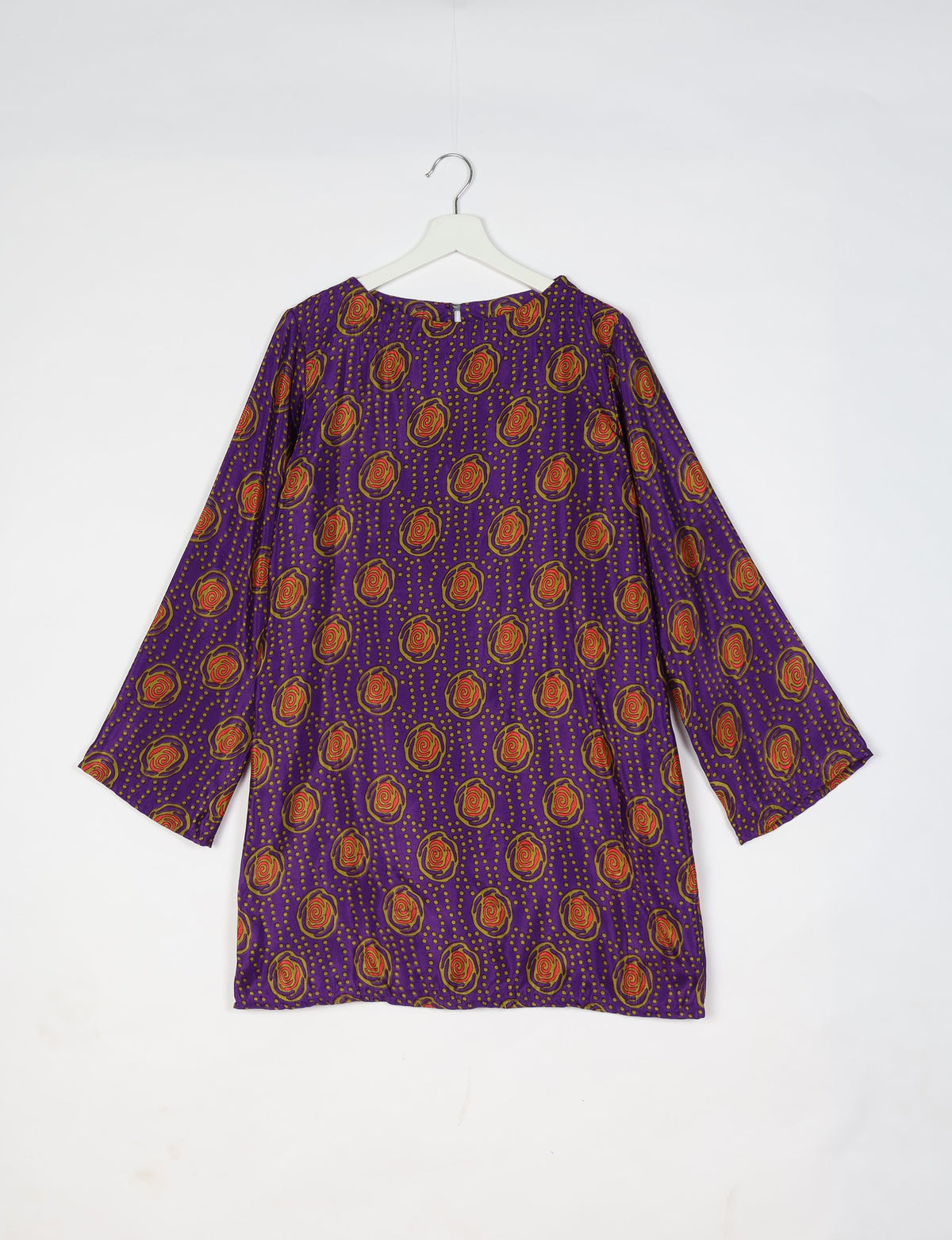 Purple swing dress with long sleeves and orange floral pattern hanging on white hanger against white background