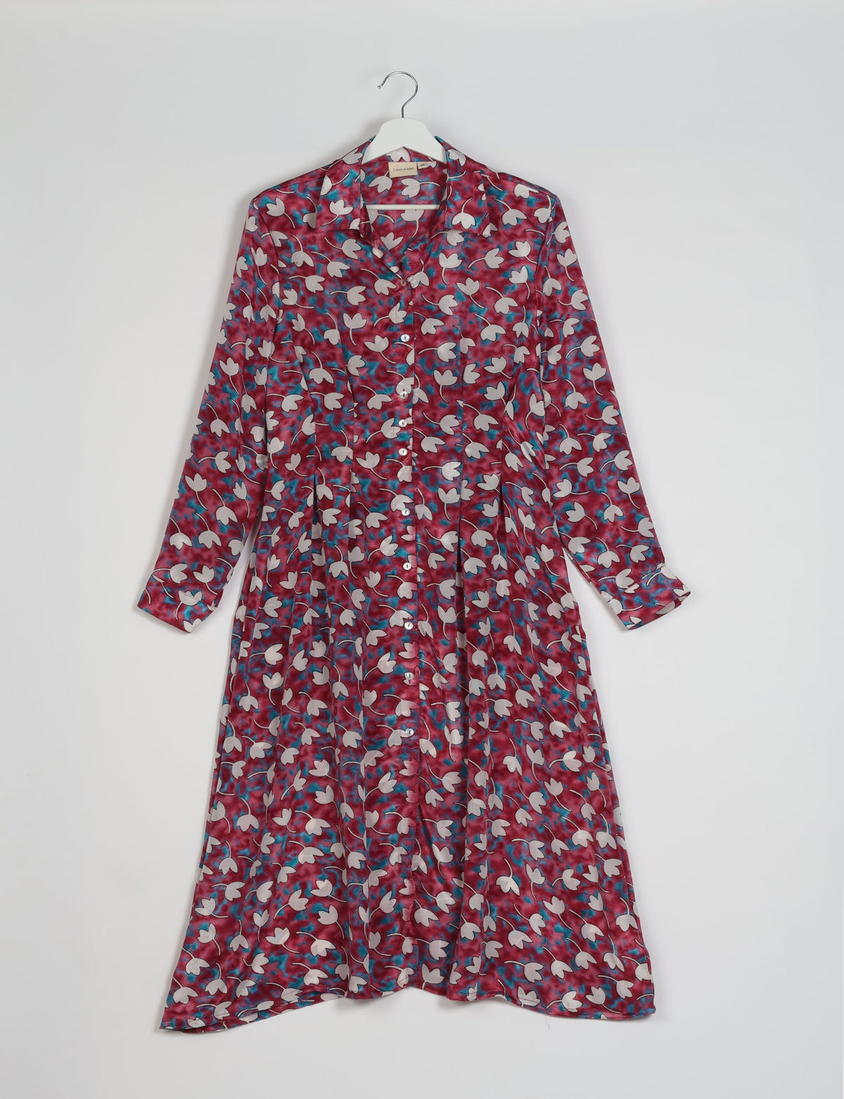 Pink floral midi shirt dress with long sleeves, button front, collar, and pleated waist, hanging on white hanger