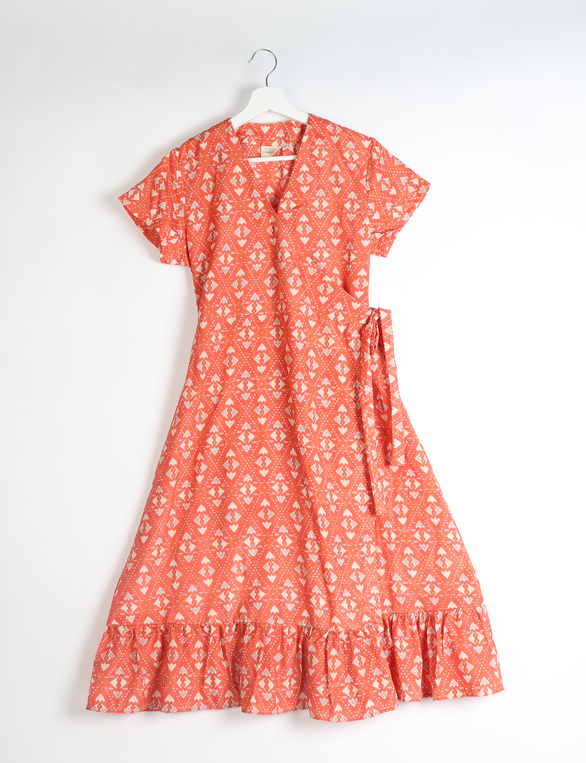 Orange midi wrap dress with white geometric pattern, short sleeves, V-neck, side tie, and ruffled hem hanging on white