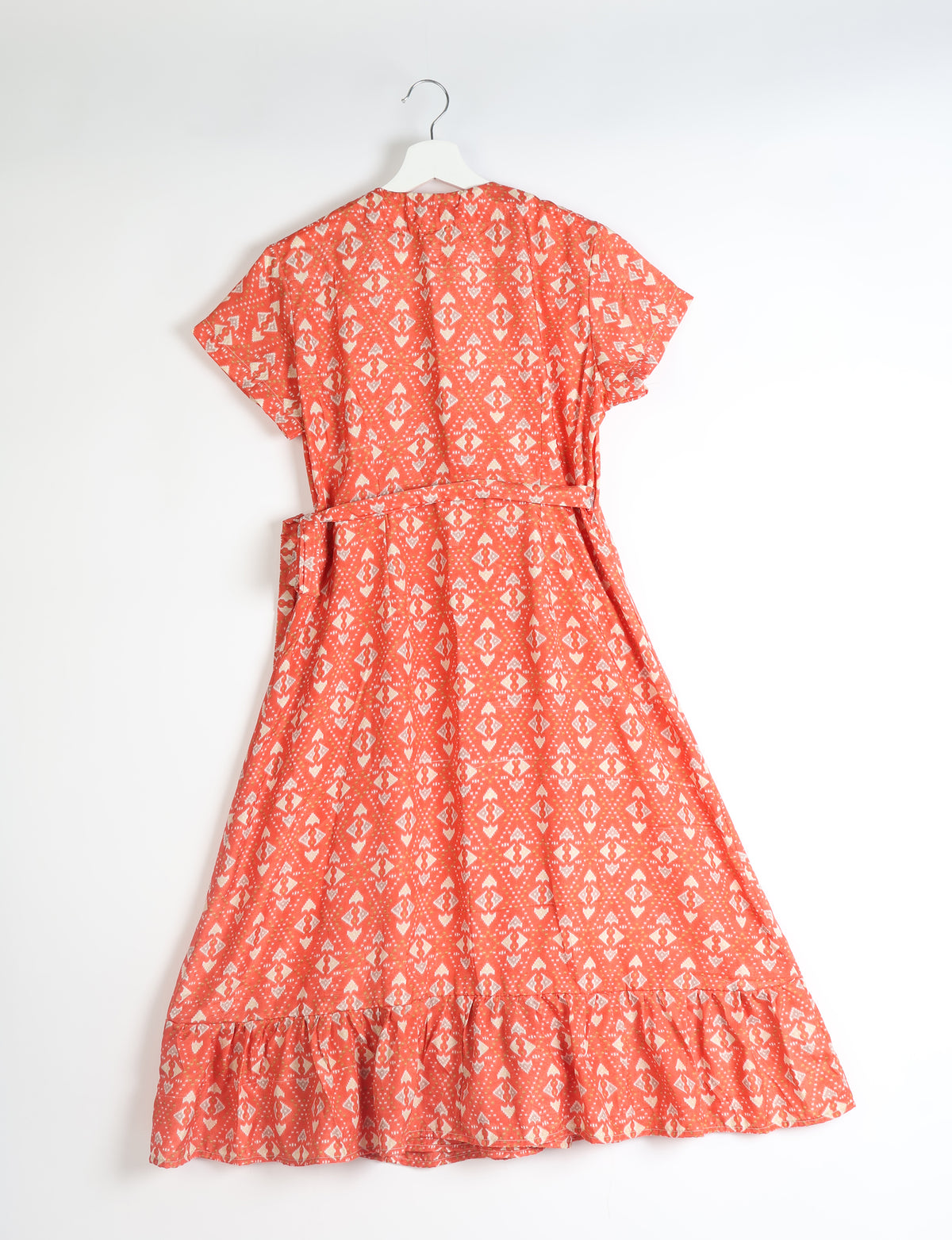 Orange midi wrap dress with white geometric pattern, short sleeves, belt, and ruffled hem, shown from back on hanger