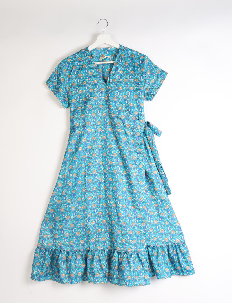 Blue tropical print midi wrap dress with short sleeves, V-neckline, side tie, and ruffled hem hanging on white hanger