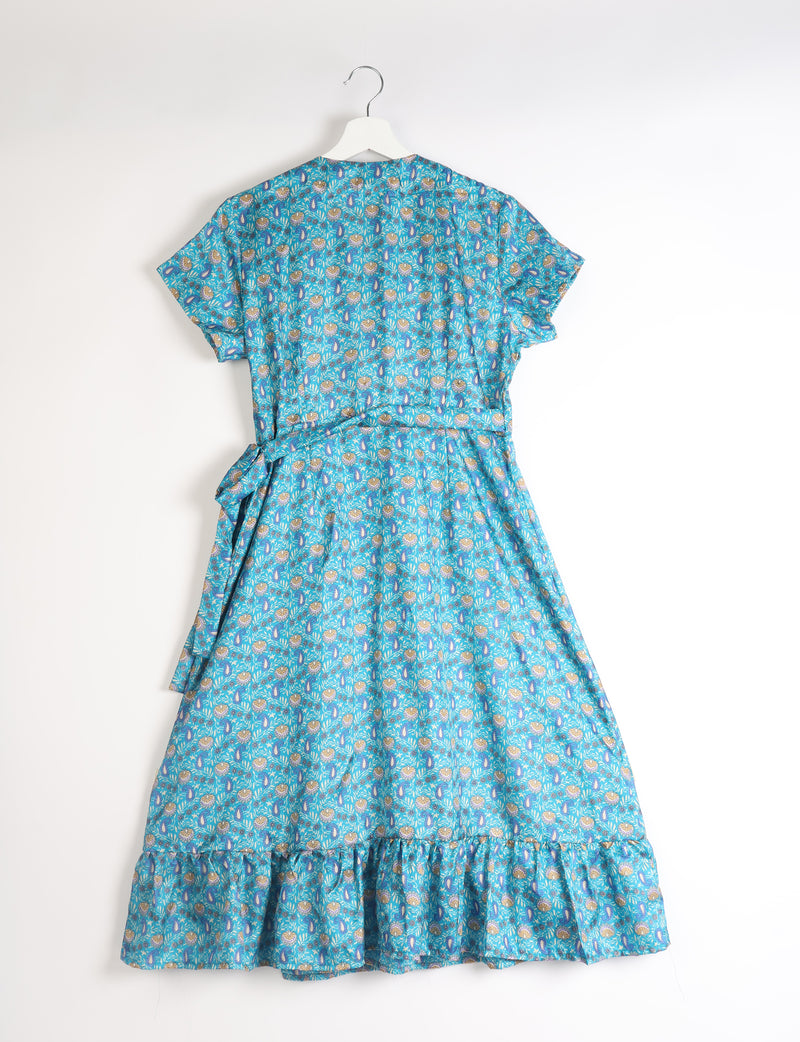 Blue tropical print midi wrap dress with short sleeves, ruffle hem, and waist tie, shown from back on white hanger