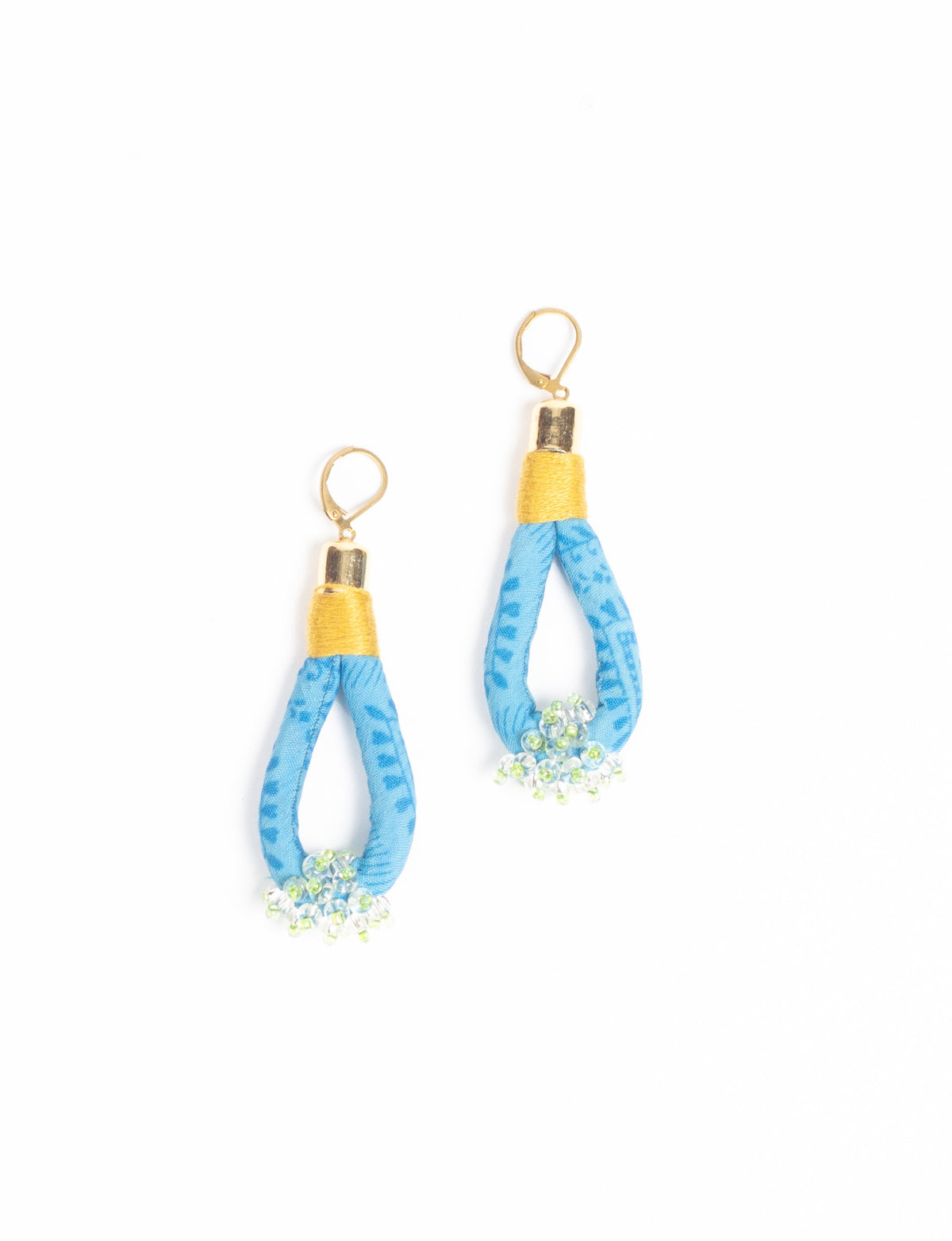 Blue fabric loop drop earrings with gold-tone tops and small clear and green beaded clusters at the bottom, flat lay view