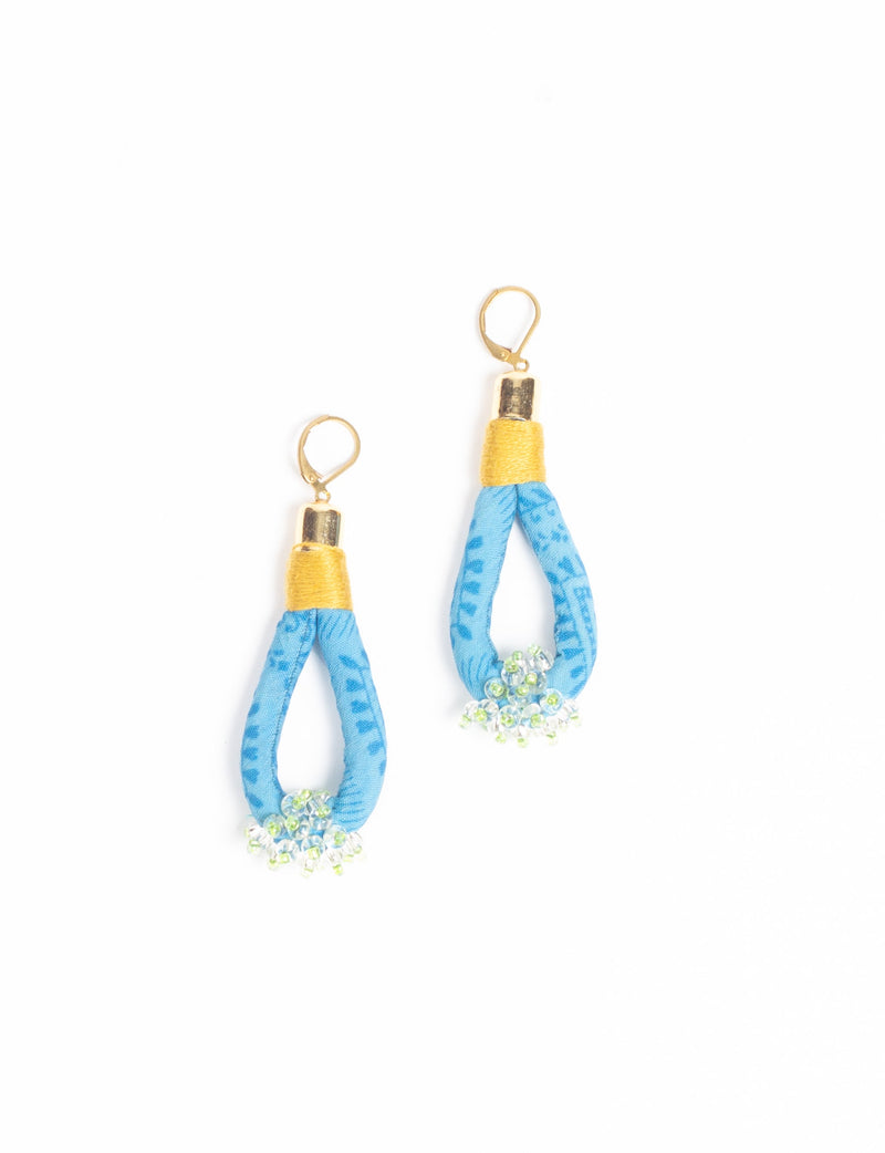 Blue fabric loop drop earrings with gold-tone tops and small clear and green beaded clusters at the bottom, flat lay view
