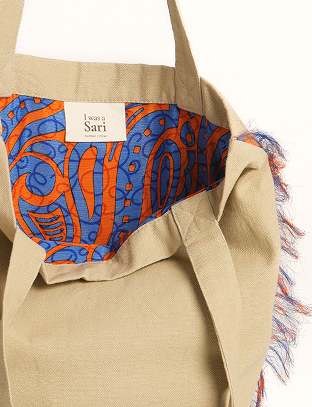 Beige canvas shopper bag with blue and orange abstract patterned lining and fringe detail on side edge