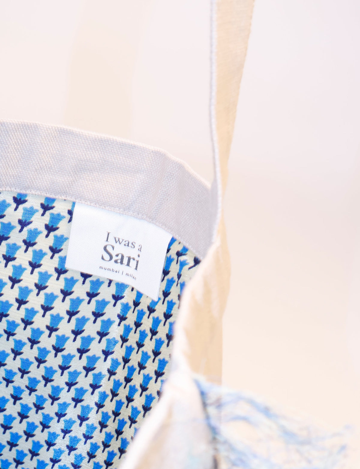 Beige shopper bag with blue floral micro pattern interior and white label reading "I was a Sari mumbai | milan"