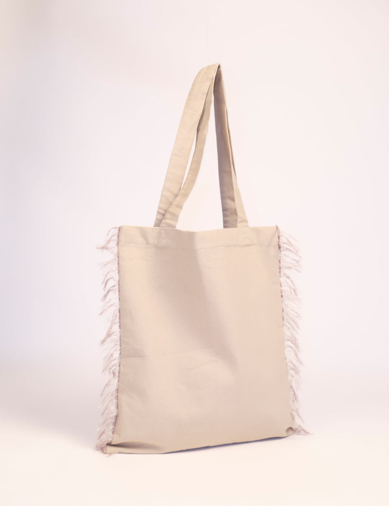 Beige fabric shopper bag with long handles and fringed sides, shown hanging against a plain background