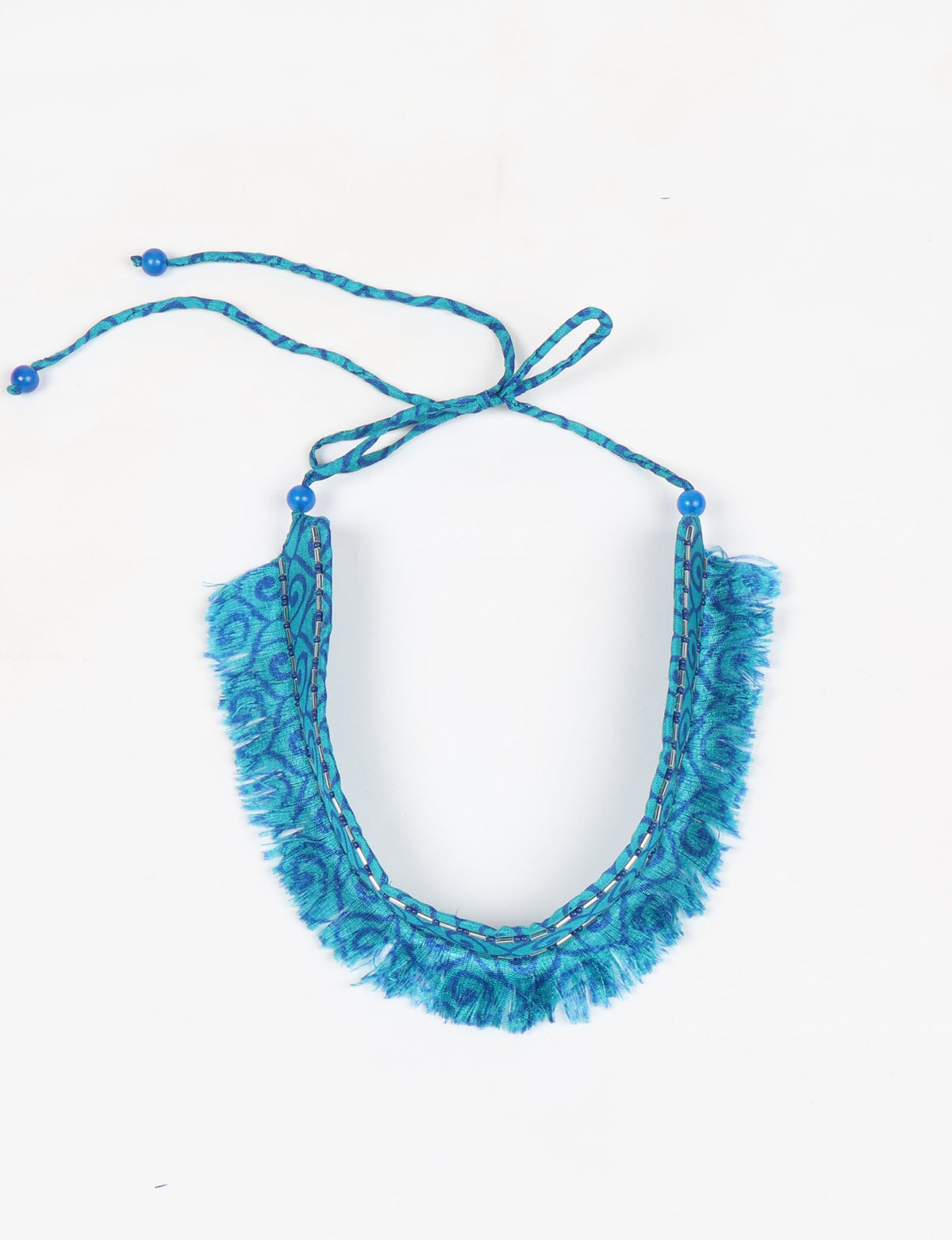 Blue abstract patterned fabric choker with fringe edges, bead accents, and tie-up closure, flat lay on white background