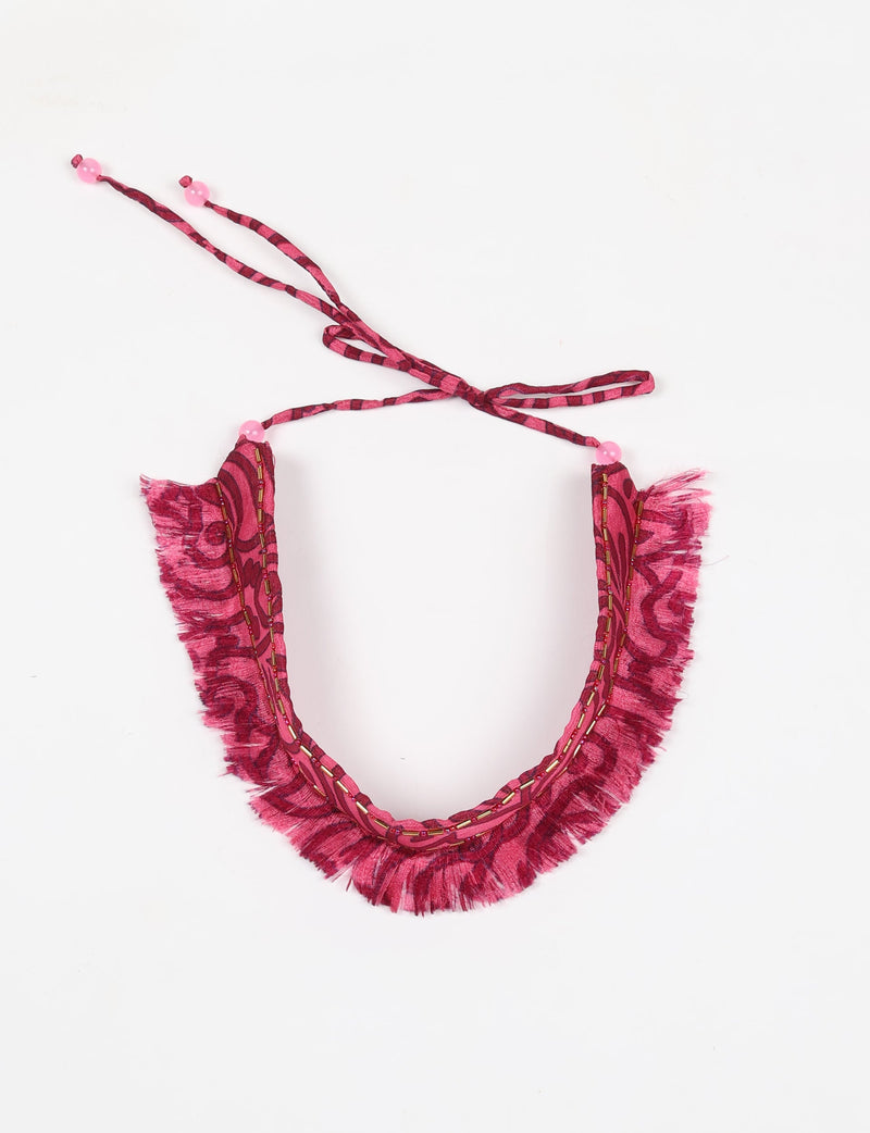 Pink abstract patterned tie-up choker with fringe edges, bead accents, and decorative stitching, shown flat on white background