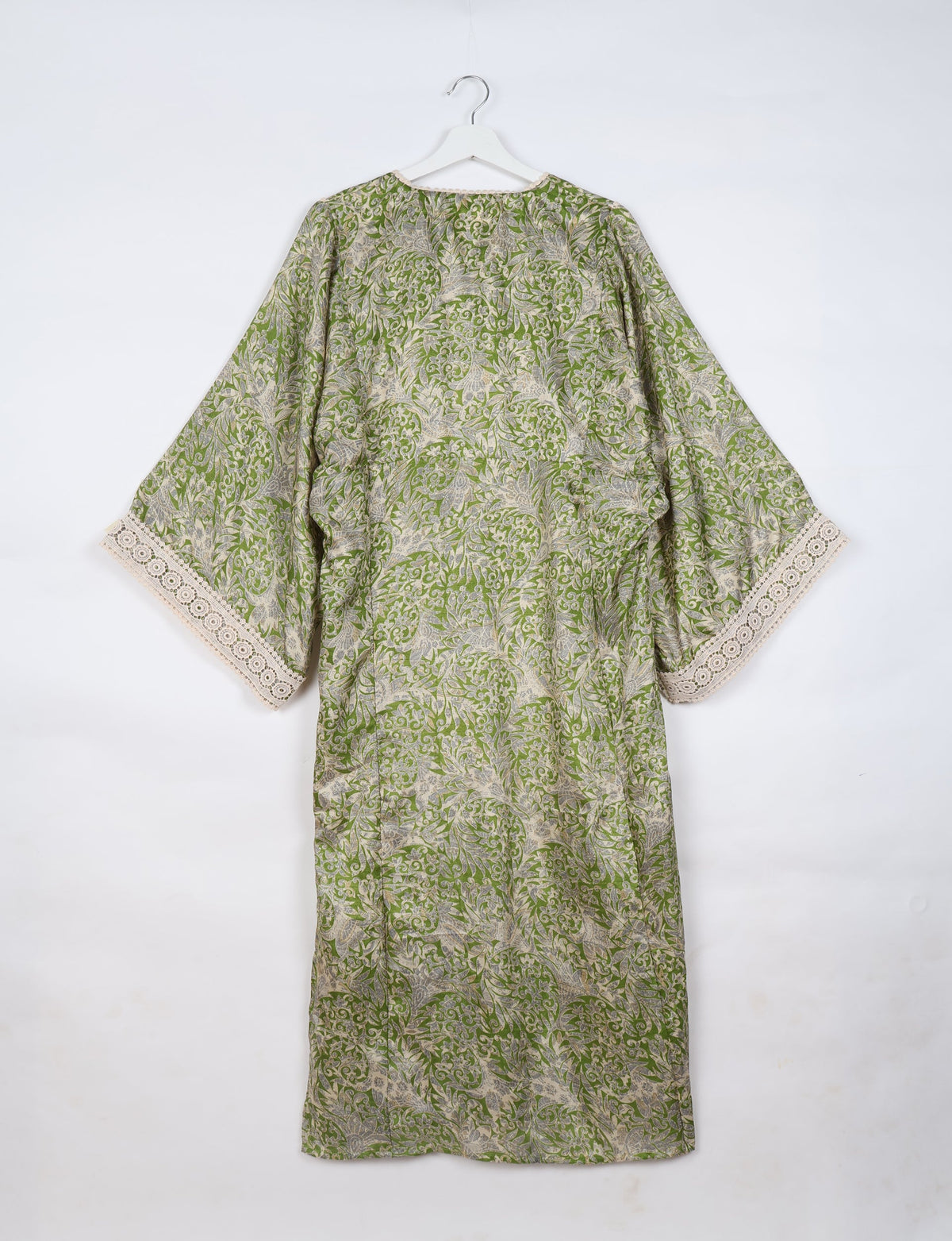 Green tropical maxi kaftan with beige and gray leaf patterns, lace trim on wide sleeves, shown hanging from white hanger