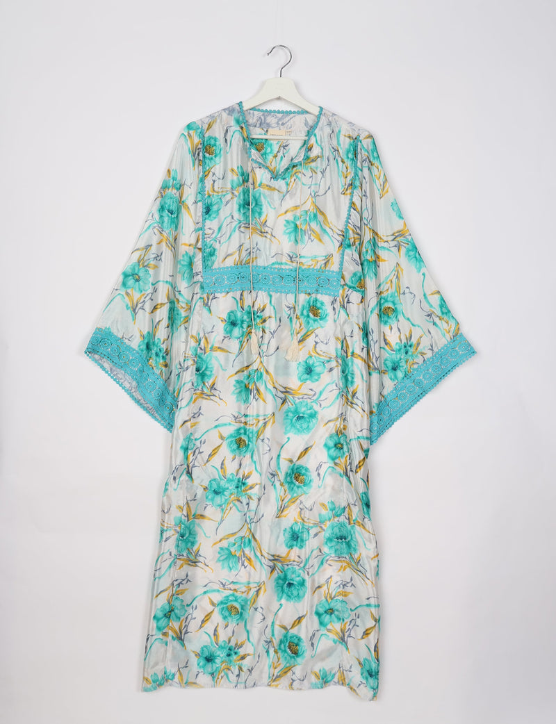 White maxi kaftan with turquoise floral print and lace trim, hanging on a white hanger against a white background