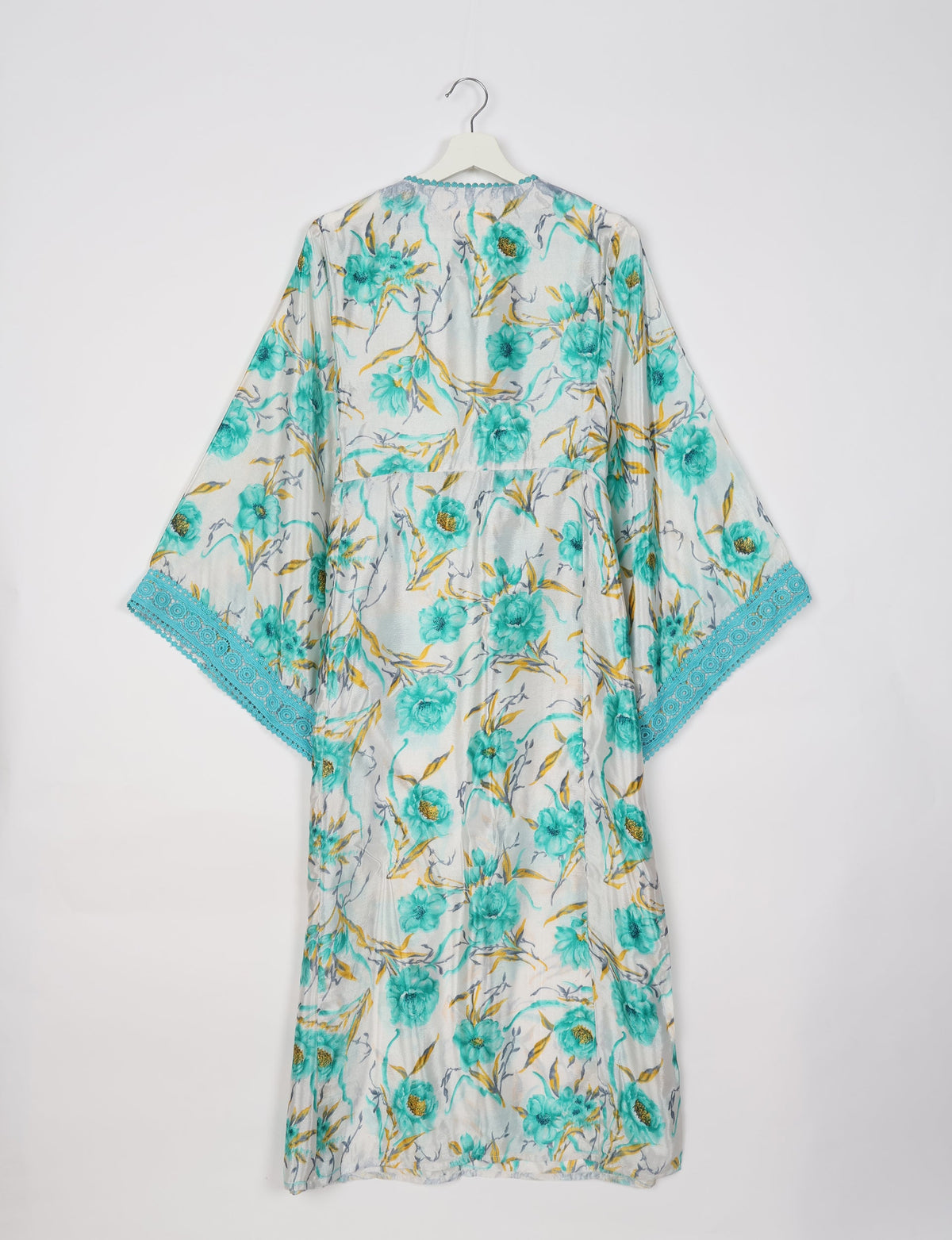 White maxi kaftan with turquoise floral print, wide sleeves, and turquoise lace trim on sleeve edges, shown hanging flat