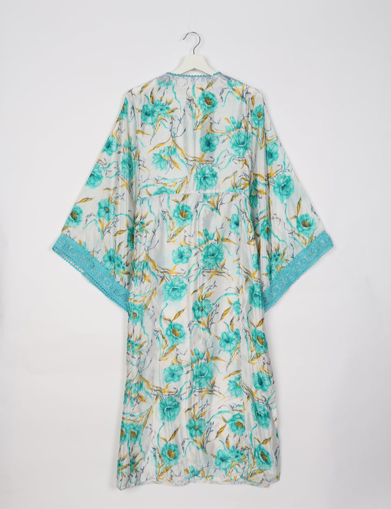White maxi kaftan with turquoise floral print, wide sleeves, and turquoise lace trim on sleeve edges, shown hanging flat