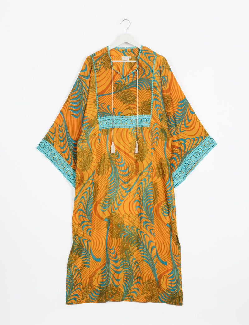 Yellow maxi kaftan with abstract blue and green patterns, blue lace trim on sleeves and chest, hanging on white hanger