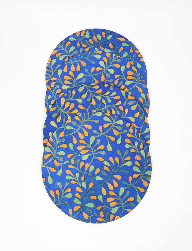 Set of four round placemats with blue background and orange and green leaf pattern, shown flat and overlapping