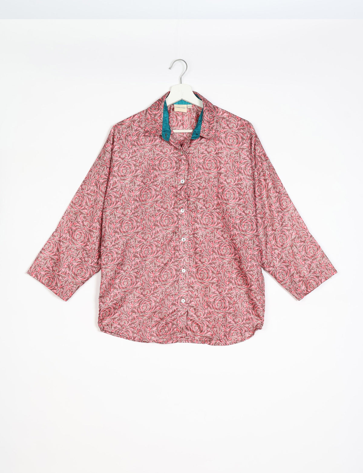 Pink oversized button-up shirt with floral swirl pattern and contrasting teal inner collar, hanging on white hanger