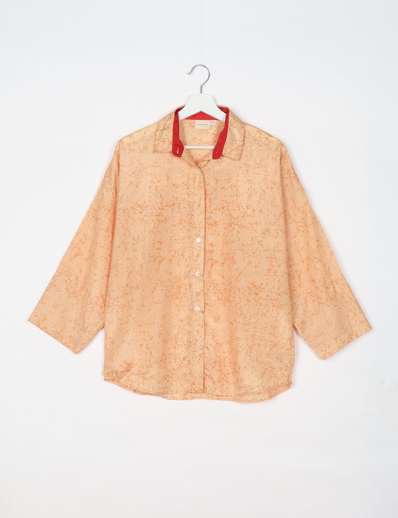 Oversized orange abstract patterned shirt with red inner collar, button front, and three-quarter sleeves hanging on white hanger