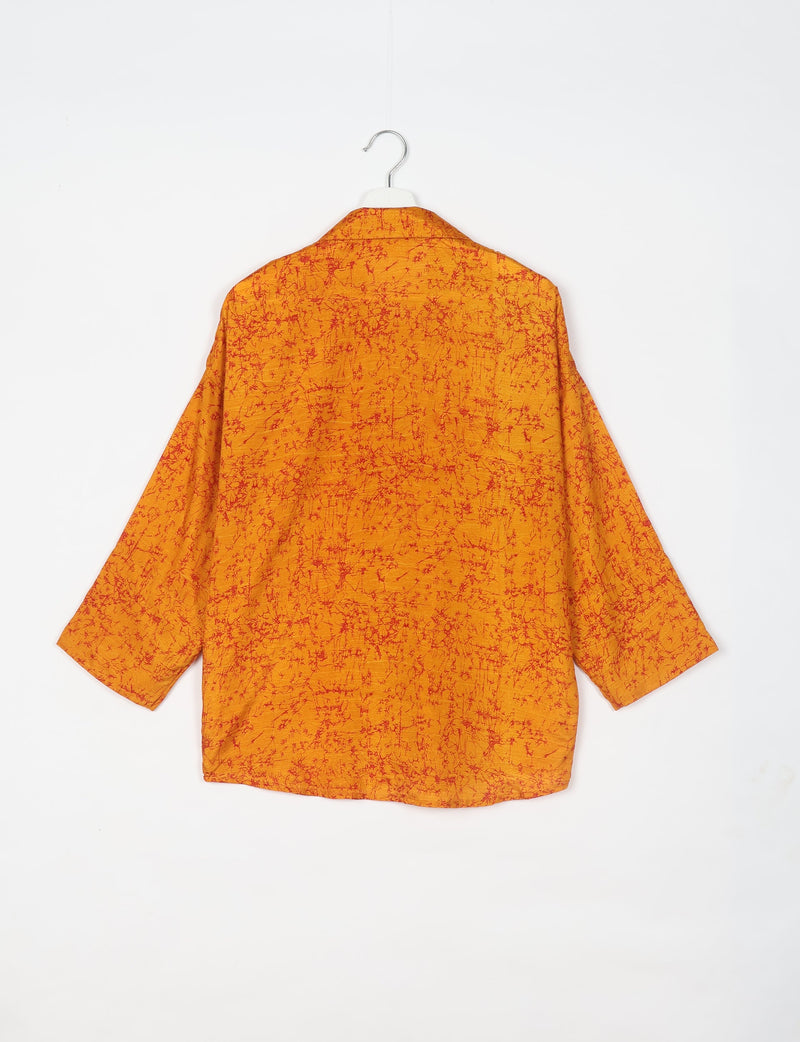 Oversized orange shirt with red abstract pattern, shown from the back, hanging on a white hanger against a white background