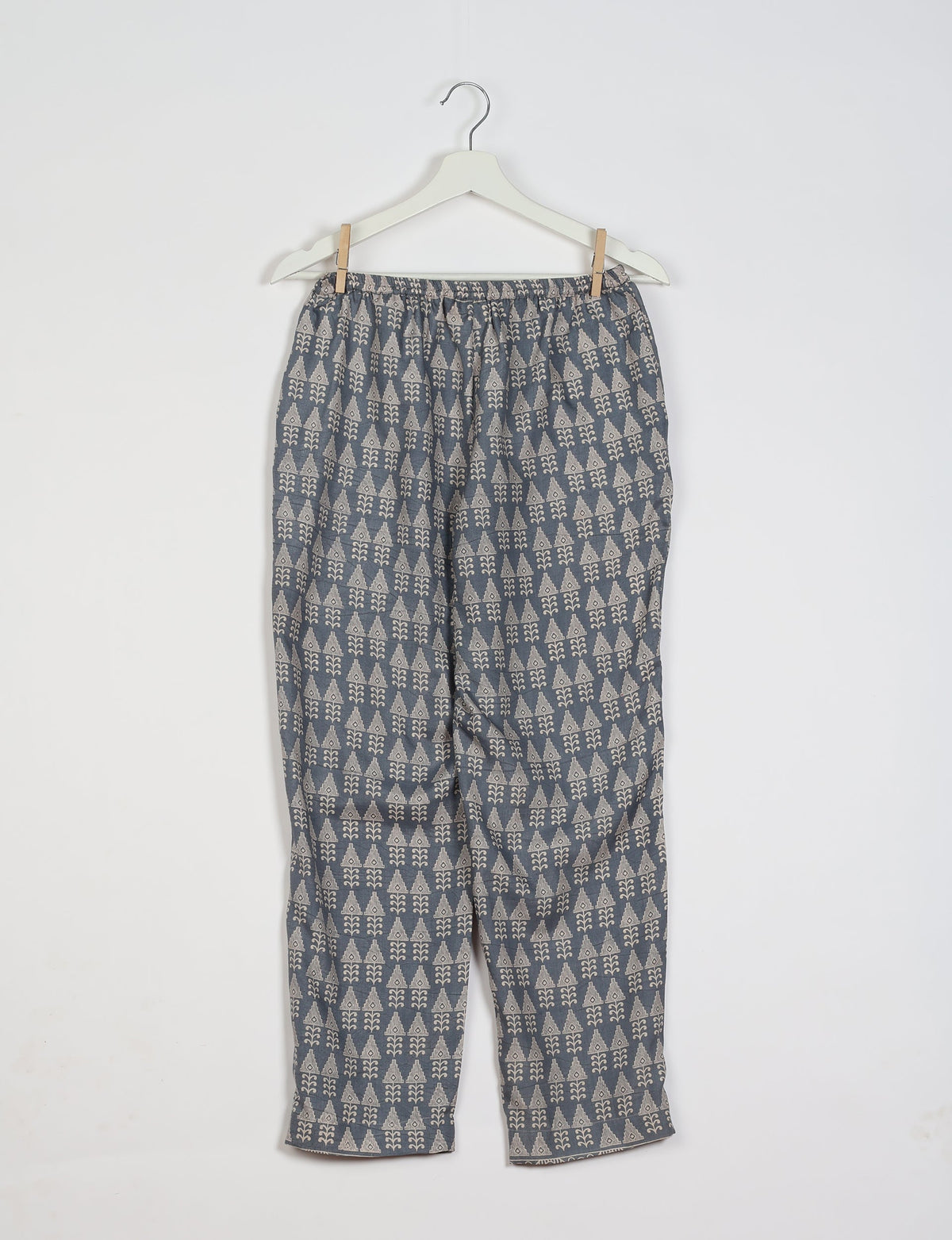 Grey pull-on pants with beige geometric pattern, elastic waistband, hanging on white hanger against white background