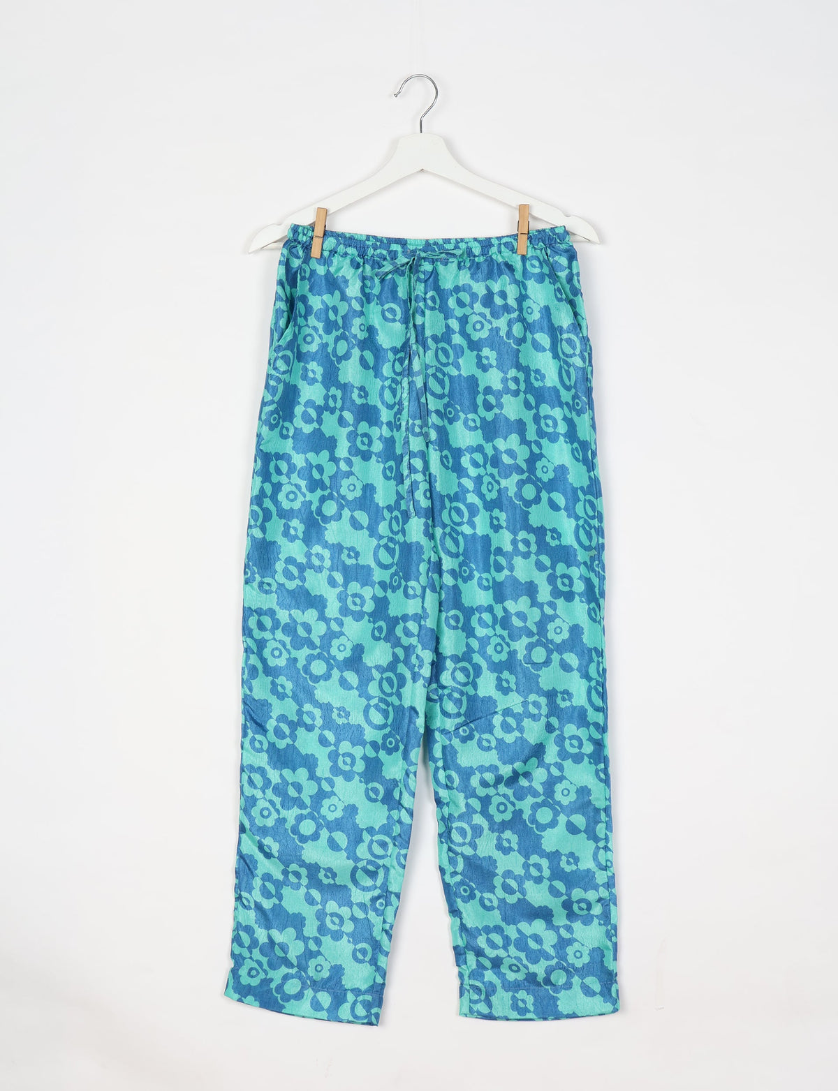 Blue floral patterned pull-on pants with elastic waistband and drawstring, hanging on white hanger, front view