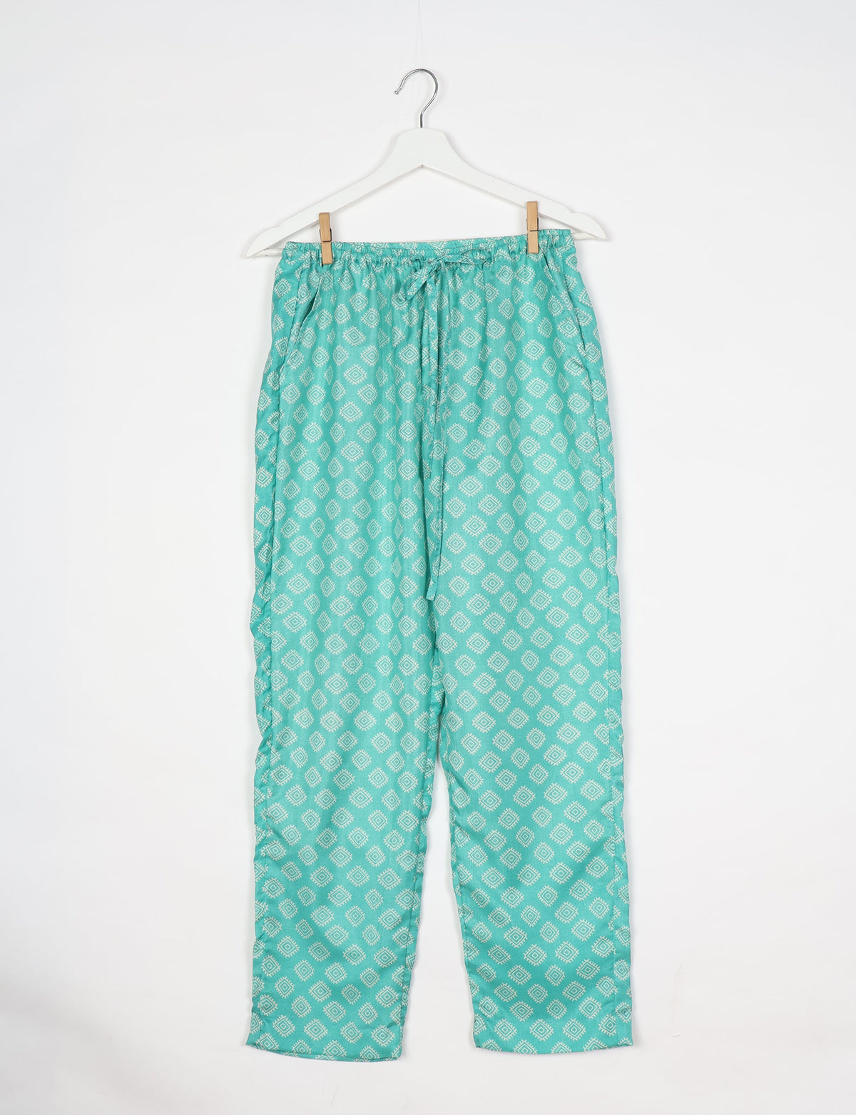 Green pull-on pants with white geometric diamond pattern, elastic waistband, and drawstring, hanging on white hanger