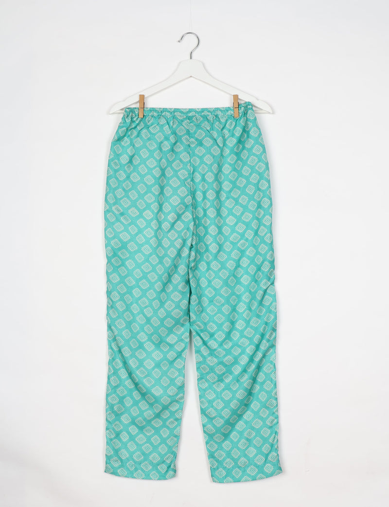 Green pull-on pants with white geometric diamond pattern hanging on white hanger against white background