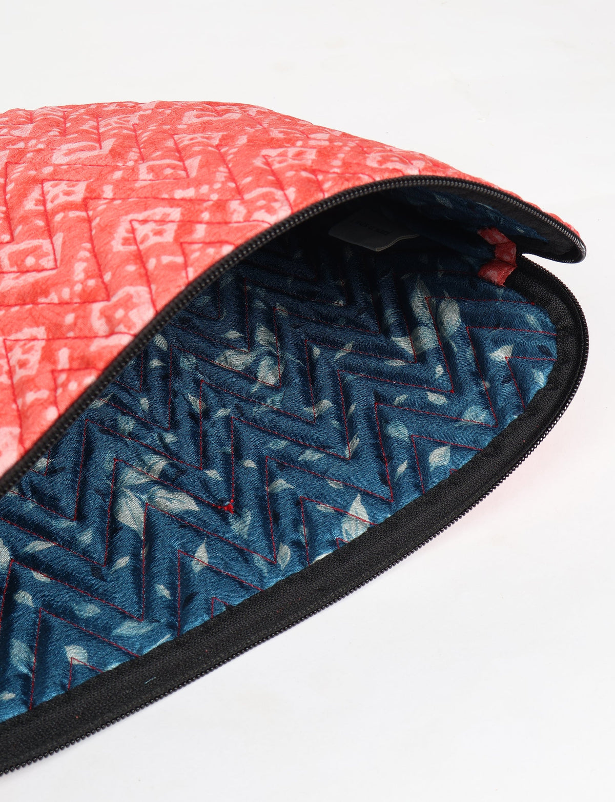 Quilted laptop sleeve with pink geometric pattern exterior and blue zigzag patterned interior, partially unzipped flat lay
