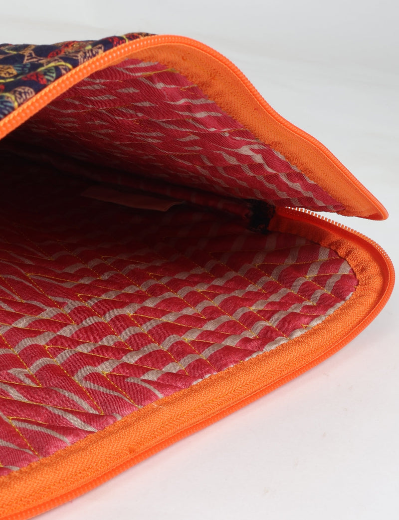 Quilted laptop sleeve with orange trim, red patterned interior, and blue tropical patterned exterior, shown open from inside view