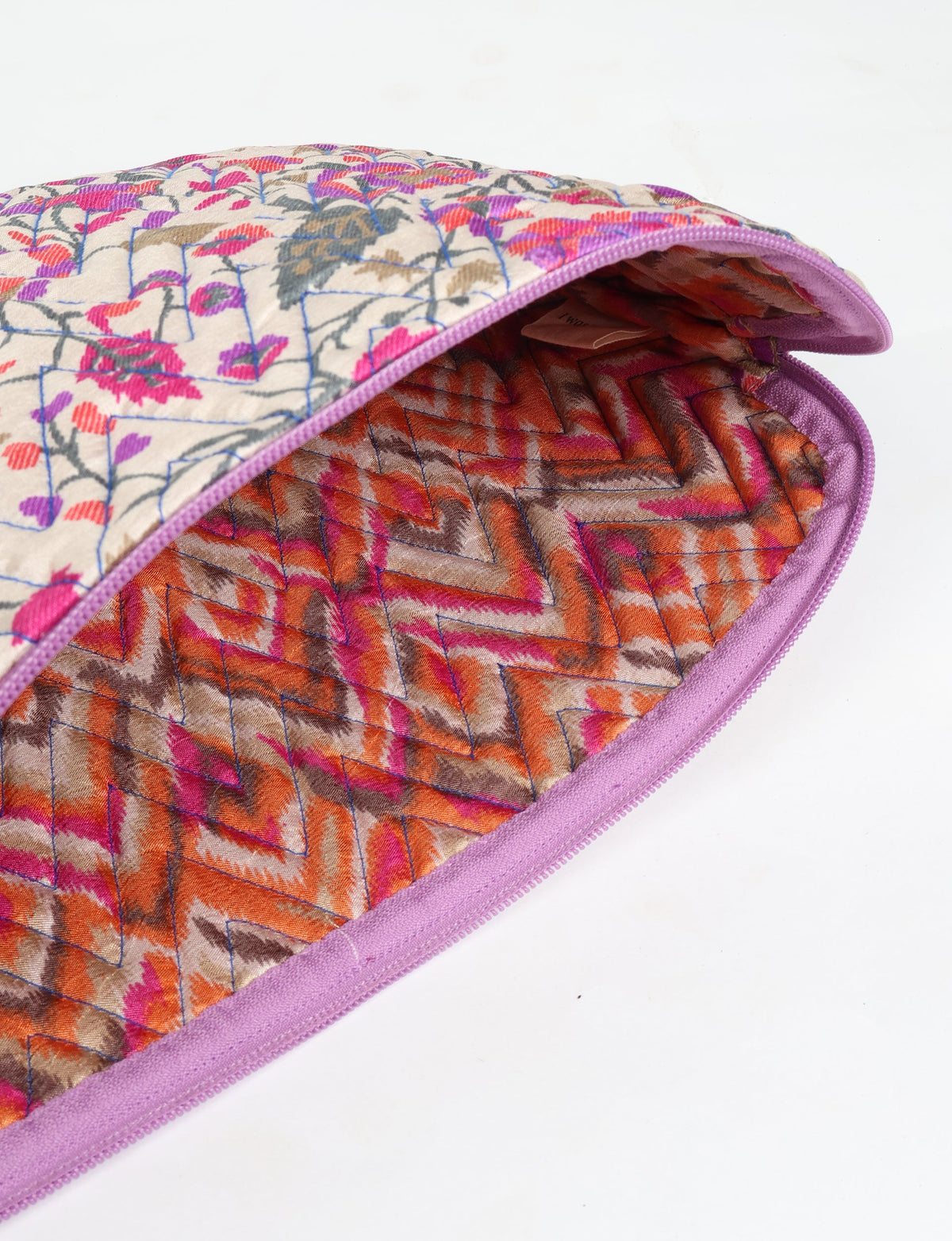 Quilted laptop sleeve with beige tropical floral exterior and orange-pink chevron quilted interior, purple zipper edge, flat lay