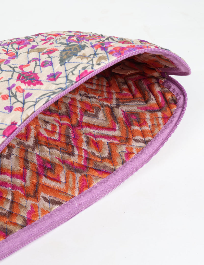 Quilted laptop sleeve with beige tropical floral exterior and orange-pink chevron quilted interior, purple zipper edge, flat lay