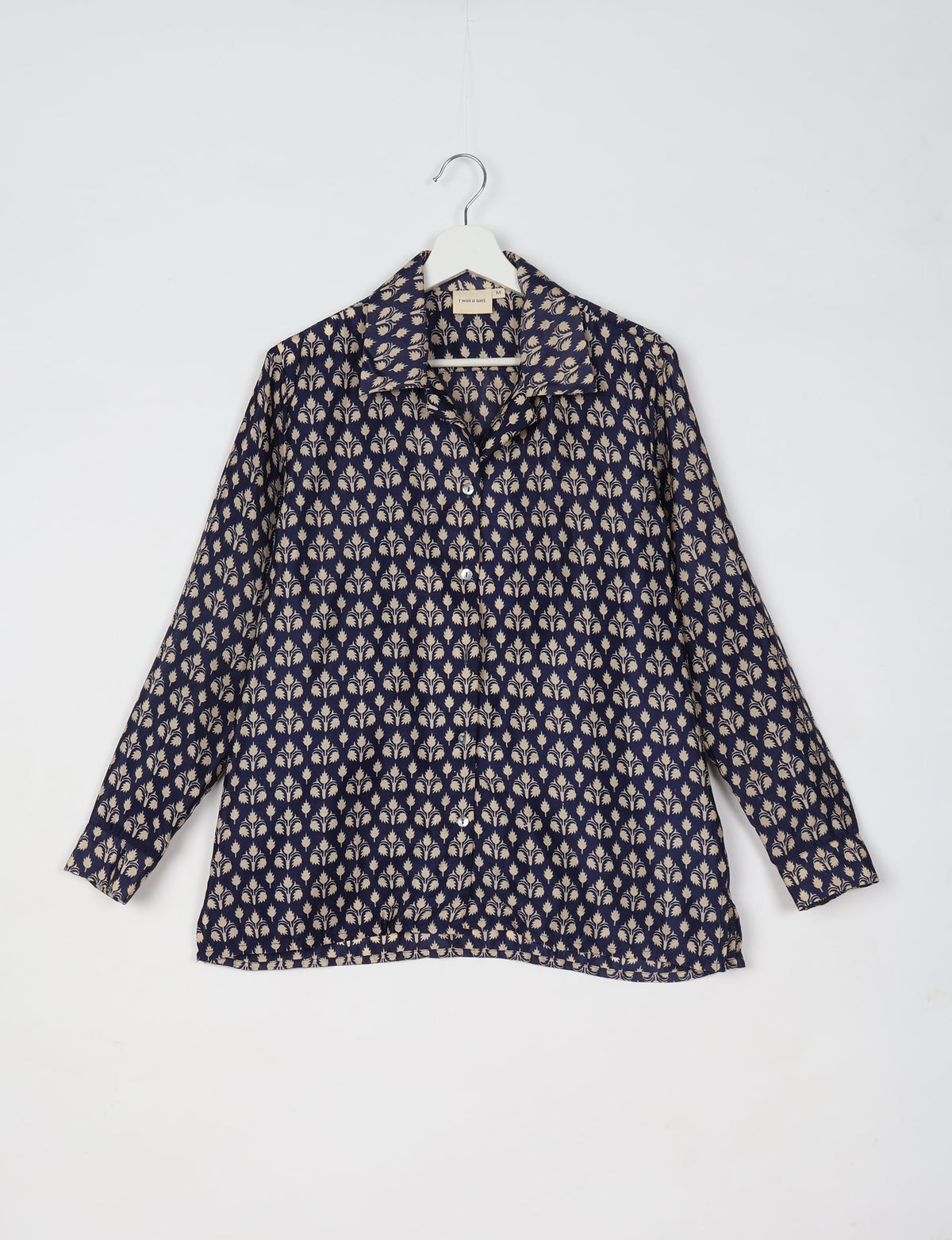 Blue resort shirt with beige micro floral design, long sleeves, button front, and collar, hanging on white hanger