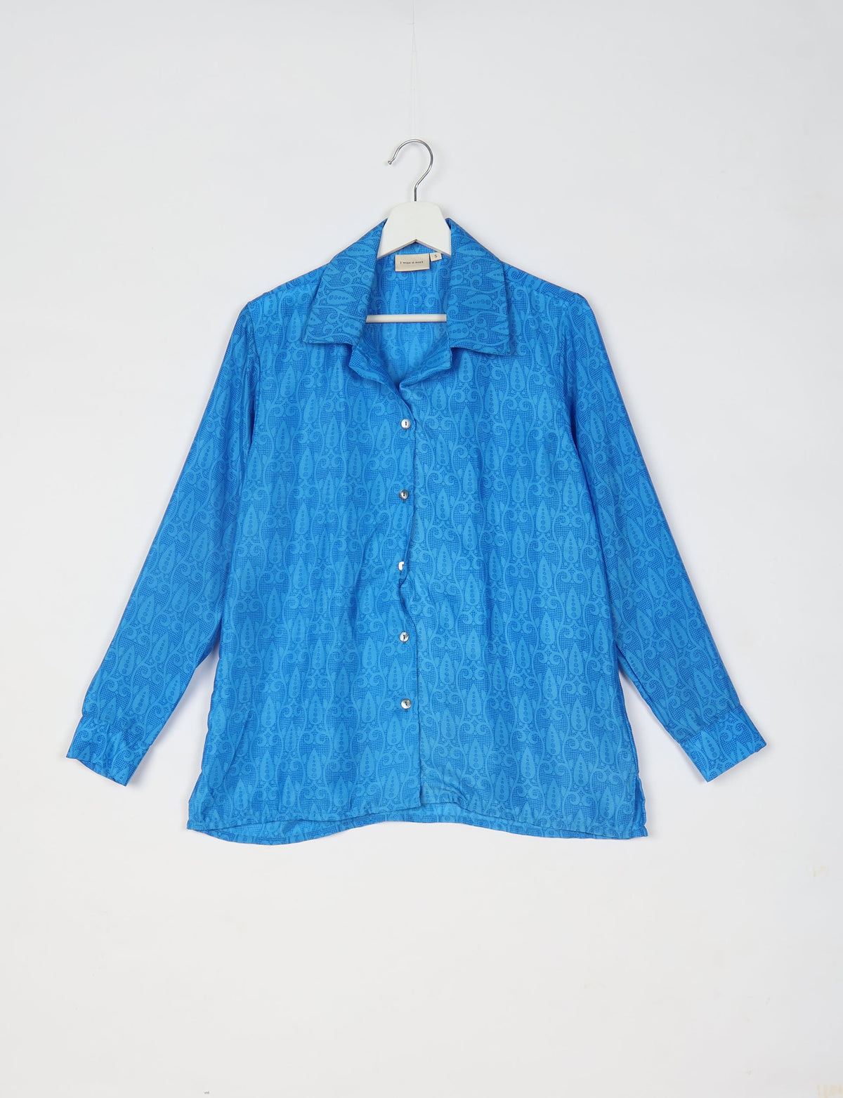 Blue long-sleeve button-up resort shirt with subtle tropical pattern, spread collar, and cuffed sleeves hanging on white hanger