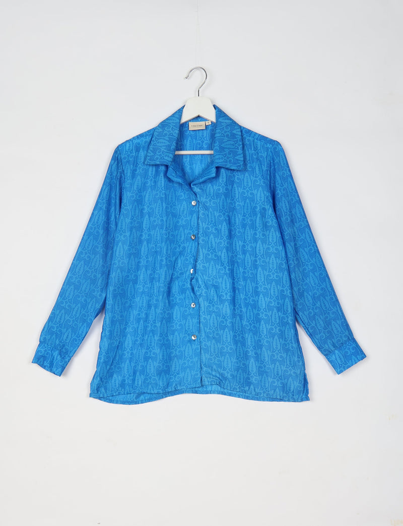 Blue long-sleeve button-up resort shirt with subtle tropical pattern, spread collar, and cuffed sleeves hanging on white hanger