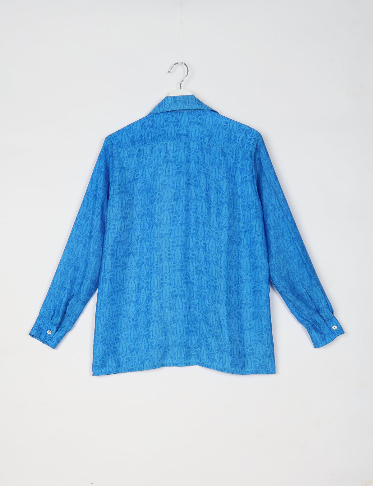 Blue long-sleeve resort shirt with tropical pattern, buttoned cuffs, and spread collar, shown from back on hanger