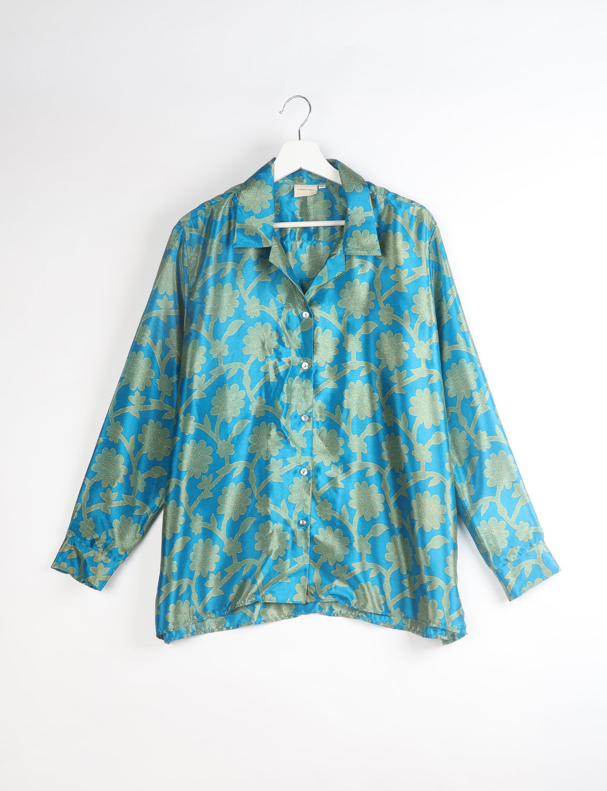 Blue floral resort shirt with long sleeves and button front, shown hanging on white hanger against white background